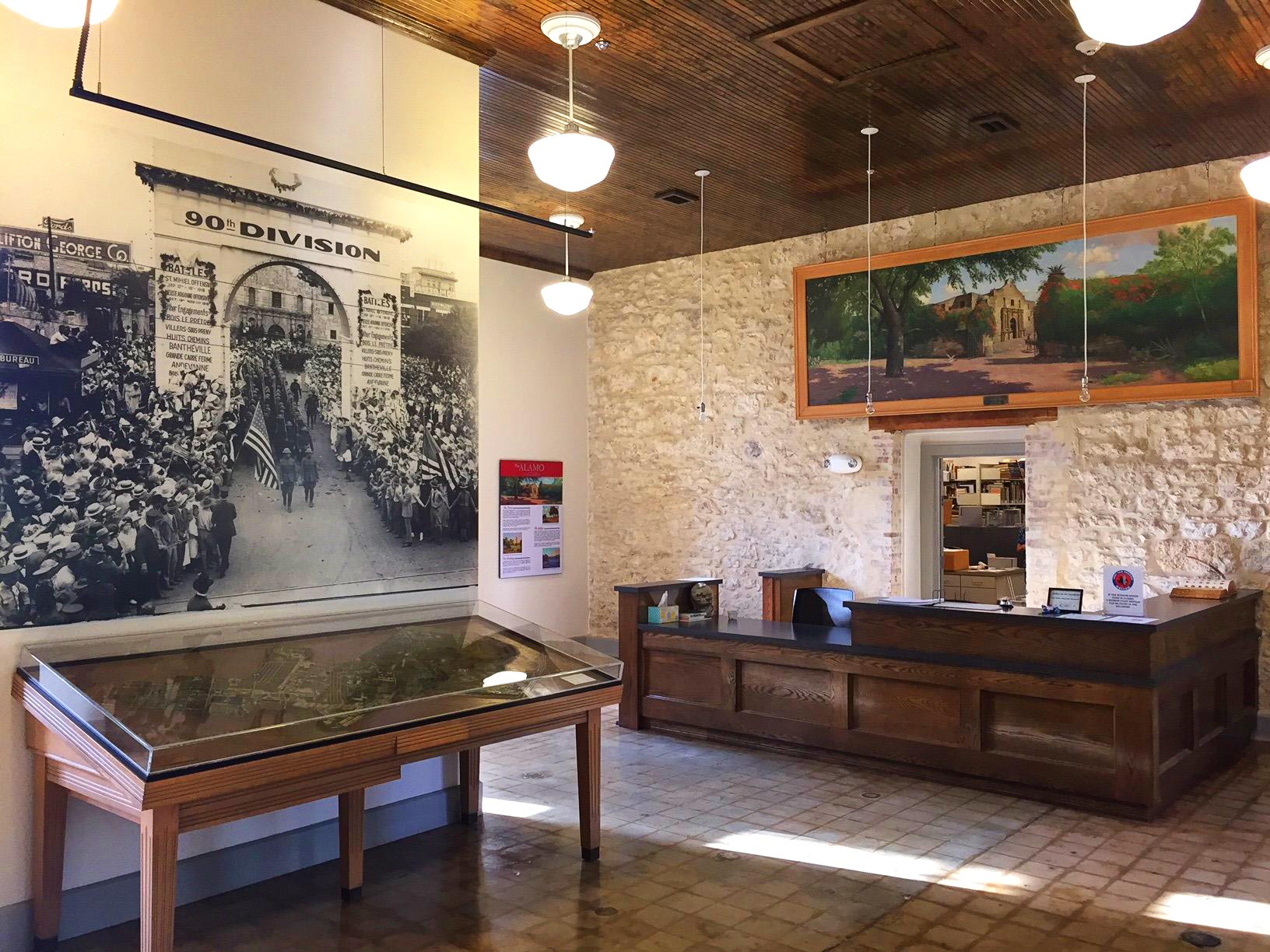 Room at the Fort Sam Houston Museum including an information desk and a museum exhibit alongside a wall in a glass enclosure.